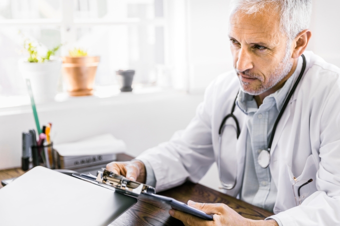 Thoughtful male doctor holding clipboard at desk